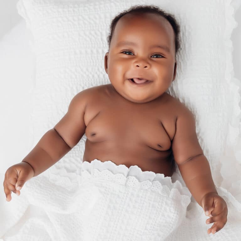 Bébé souriant allongé sur un drap blanc pendant sa séance photo éveil