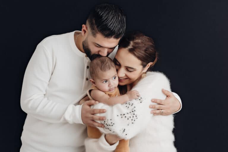 Parents tenant leur bébé de 2 mois dans les bras sur fond noir, portrait de famille en studio