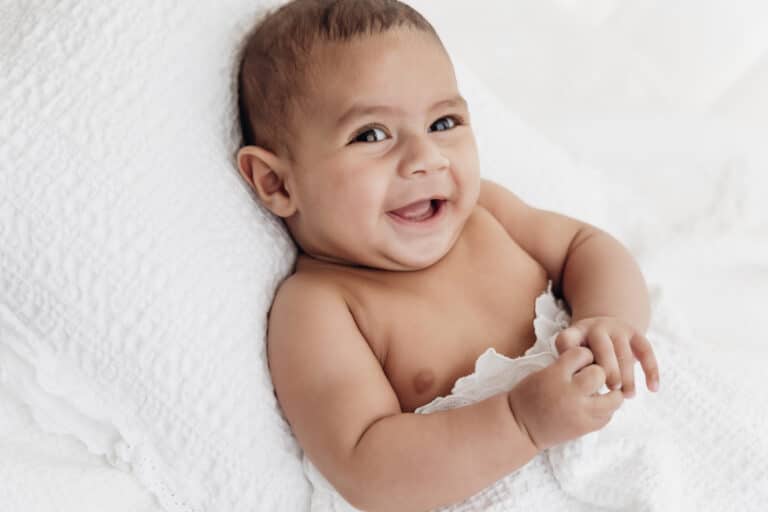 Bébé de 2 mois éveillé et souriant, allongé sur un coussin blanc, séance photo bébé éveil