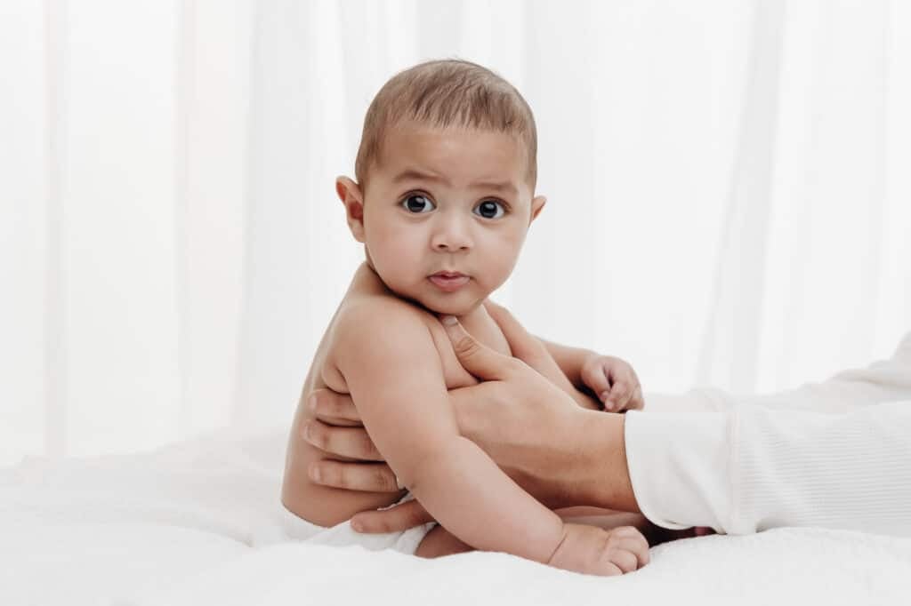 Bébé de 3 mois éveillé, assis sur un drap blanc, séance photo éveil au studio