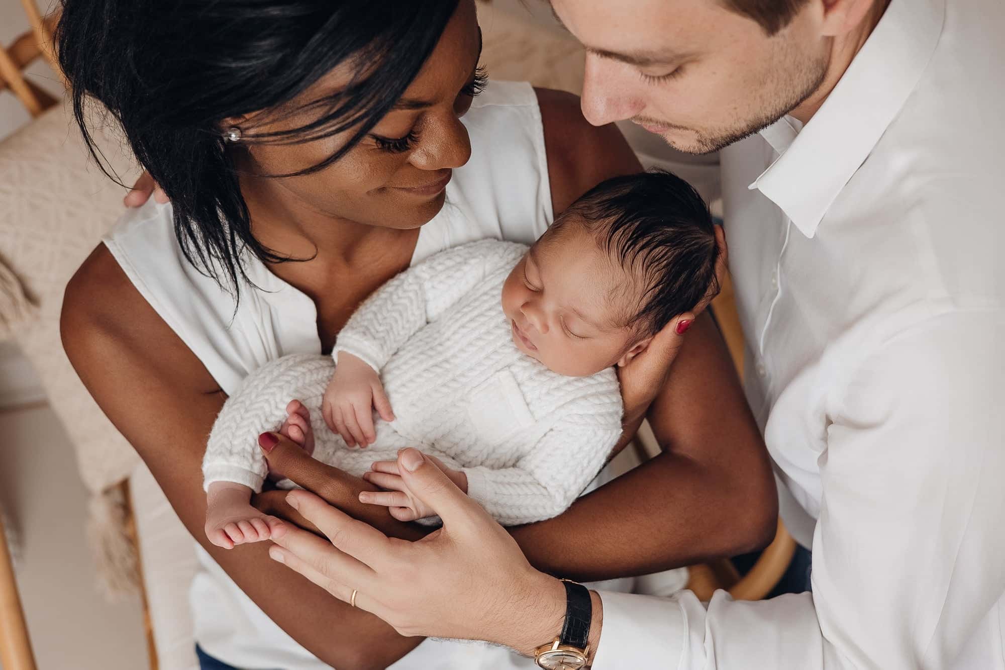 Famille tenant un bébé endormi, moments tendres en studio, entourée par les parents, ambiance douce et lumineuse. Séance photo bébé idées et préparation évoquée.