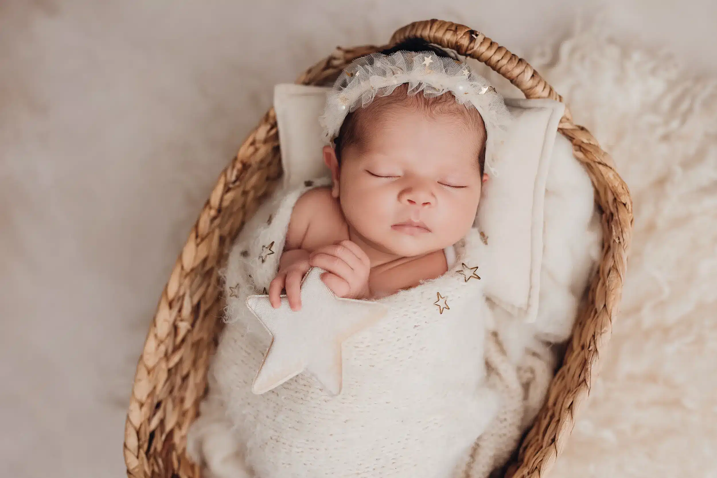 Bébé endormi dans un berceau en osier, enveloppé dans une couverture blanche, avec une étoile en tricot et un halo de dentelle sur la tête.
