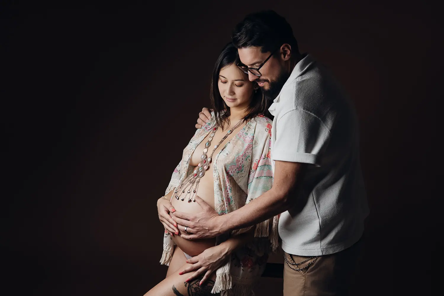 Gros plan d’un couple enceinte, l’homme caresse le ventre de la future maman, douceur et complicité dans une séance grossesse chaleureuse.