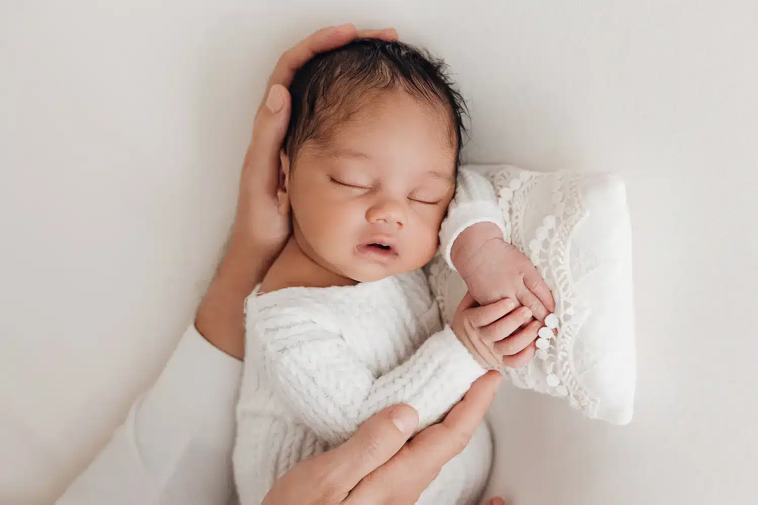Nouveau-né dormant dans les bras d’un parent, main soutenant sa tête et son petit pied enveloppé.