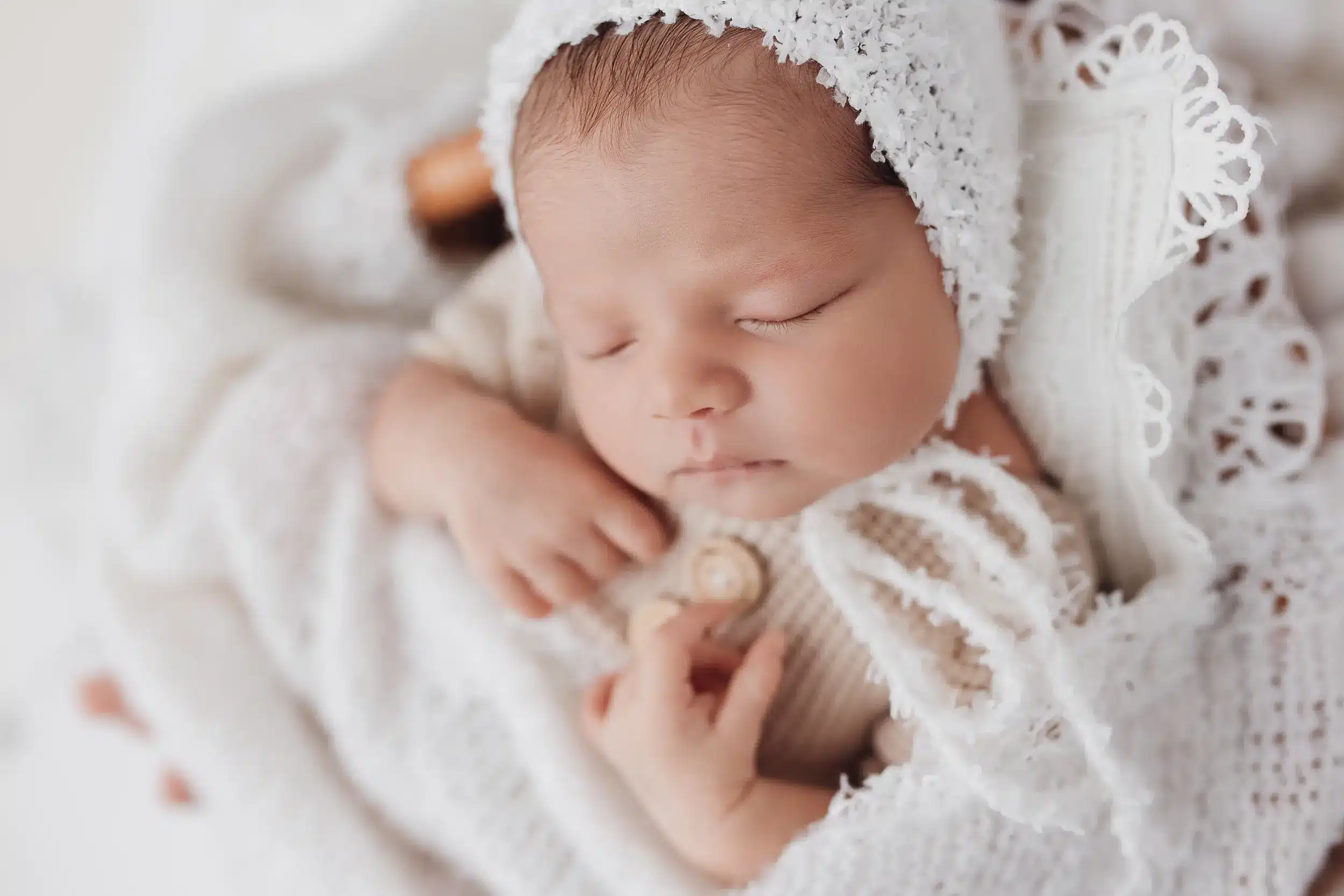 Nouveau-né endormi, petit bébé en layette blanche et bonnet dentelle, posé paisiblement.