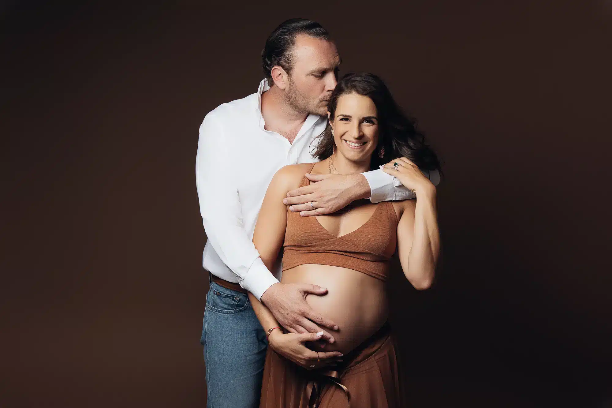 Portrait de couple enceinte: homme et femme souriants, main sur le ventre, fond vert. Idéal pour présentation grossesse.