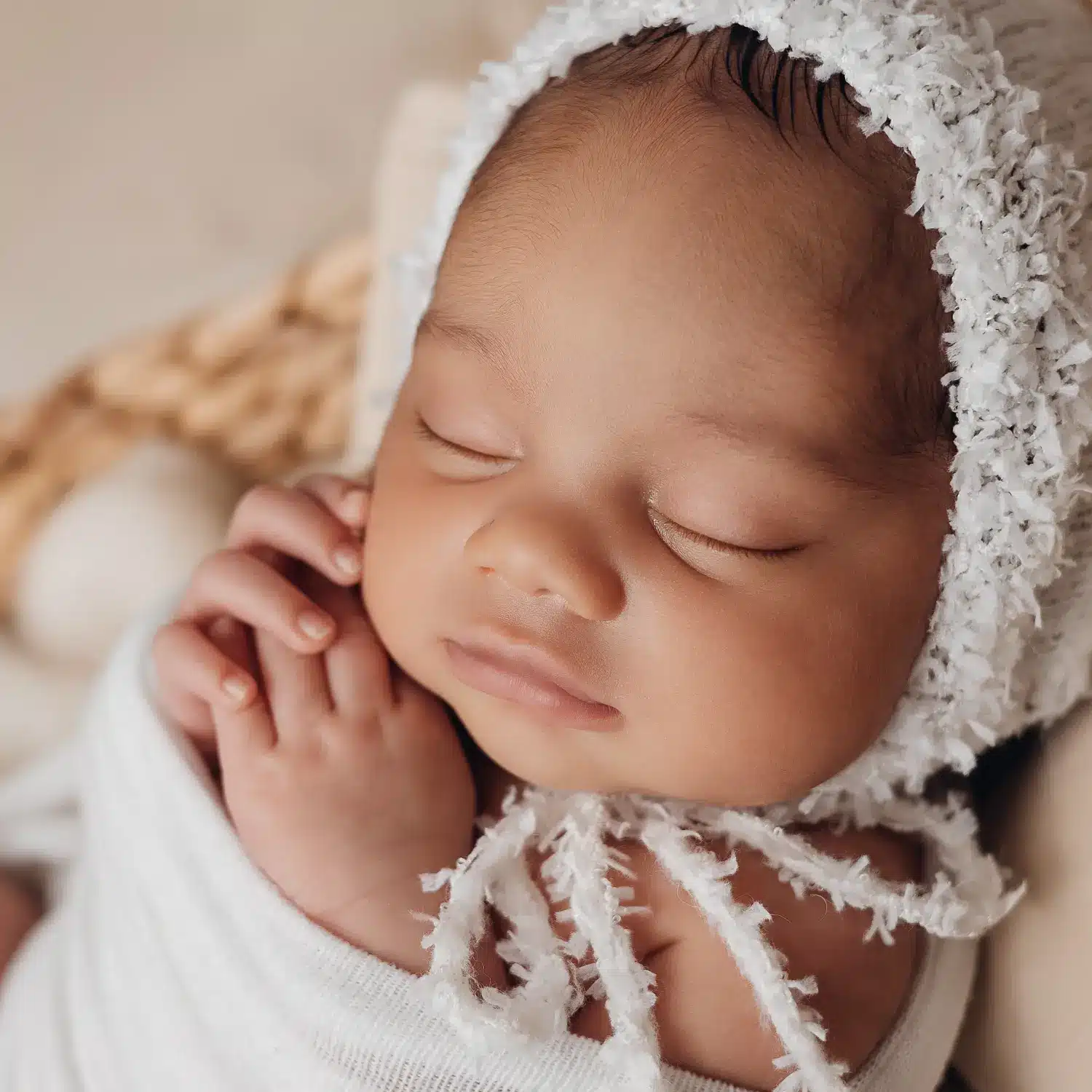 Rêveur bébé endormi, tête coiffée d'un bonnet en laine, petites mains jointes près du visage, douceur et tendresse.