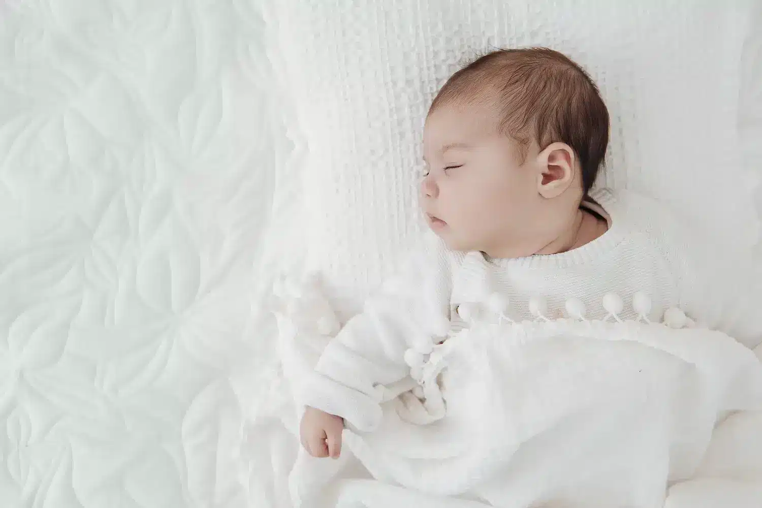 Berceau de bébé endormi sur drap clair, douceur et lumière naturelles, cadre minimal pour de belles photos de bébé à la maison.