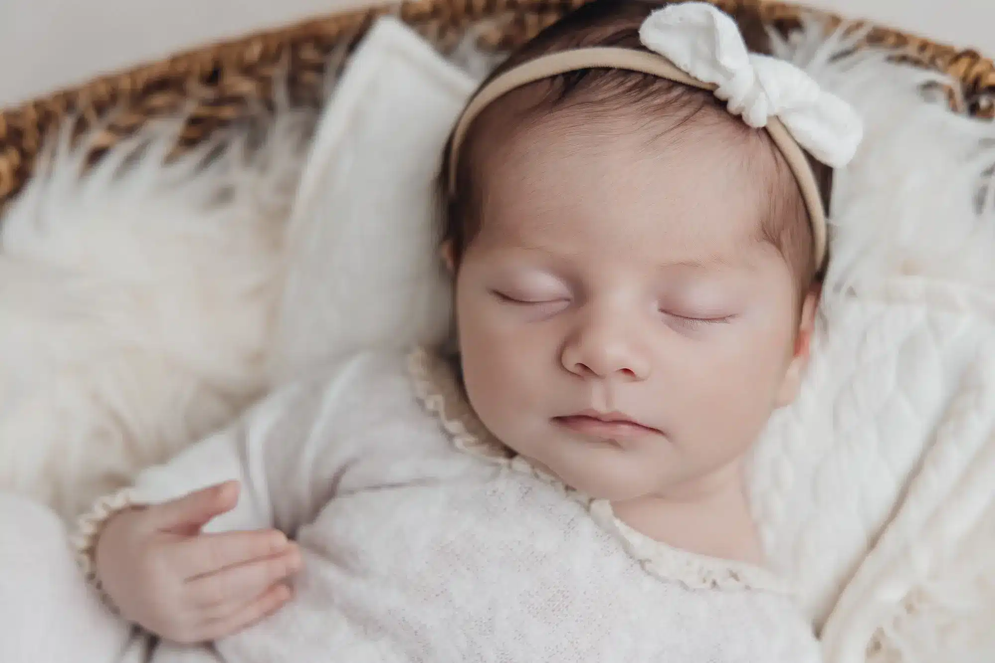 Bébé endormi, headband blanc et robe légère, blotti sur des couvertures douces dans un cadre feutré.