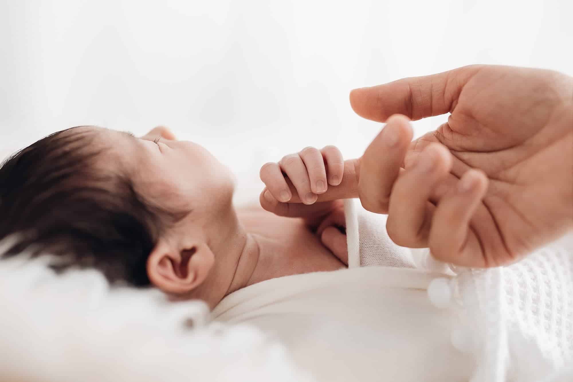 Bébé éveillé en séance photo naissance: bébé tenu par les mains, douceur et connection tendre lors d’une séance nouveau-né.