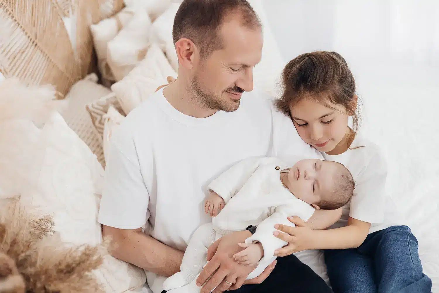 Famille heureuse avec un bébé endormi dans les bras du père et de la sœur ainée, dans un cadre lumineux et doux.