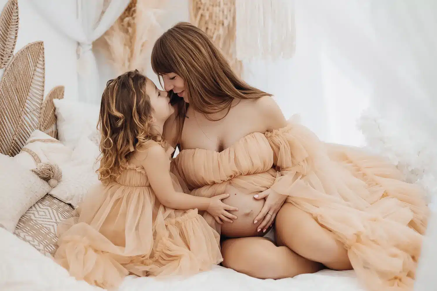 Mère enceinte et jeune fille de dos se berçant dans une ambiance douce, robe fluide couleur peau, dans un décor pastel. Alt text intégrant le mot-clé maternité pendant la grossesse.