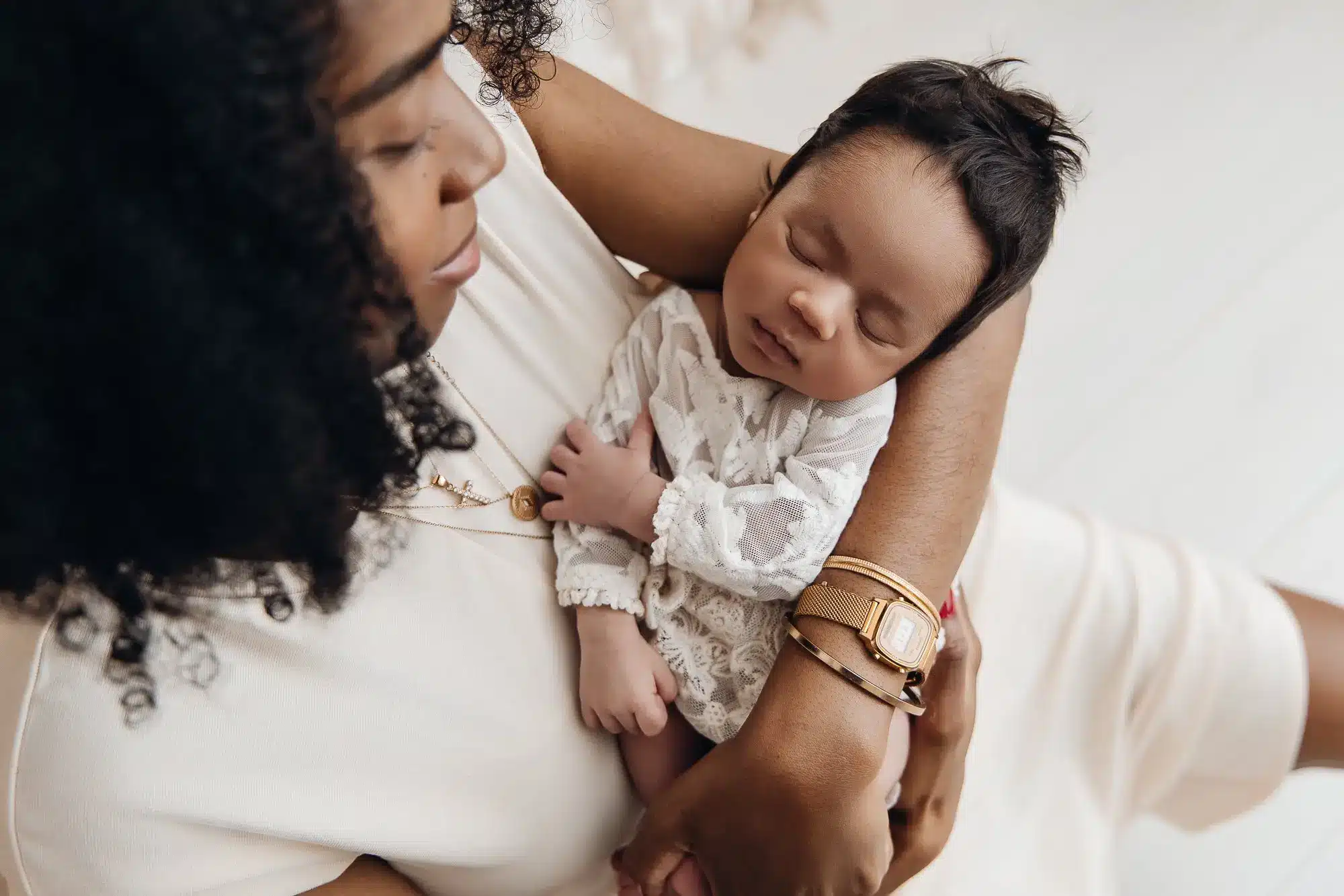Berceau-tout-petit porté contre le ventre d’une mère, bébé endormi en body blanc délicat, entouré par des bras maternels.