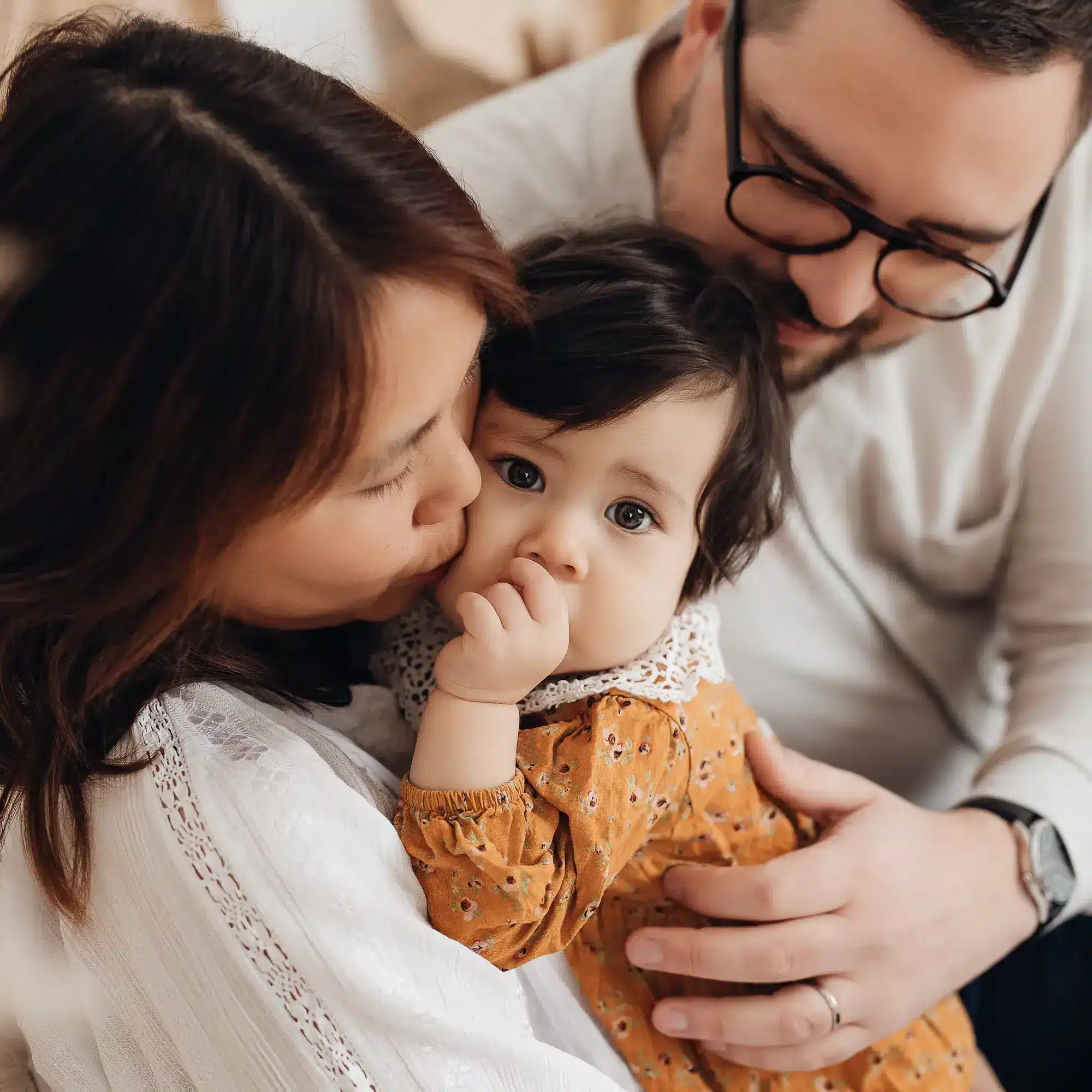 Famille réunie: un bébé au centre, entouré de ses parents qui l’embrassent tendrement dans un cadre lumineux, avec un style de vie doux. Comment faire de belles photos de son bébé avec son téléphone ?