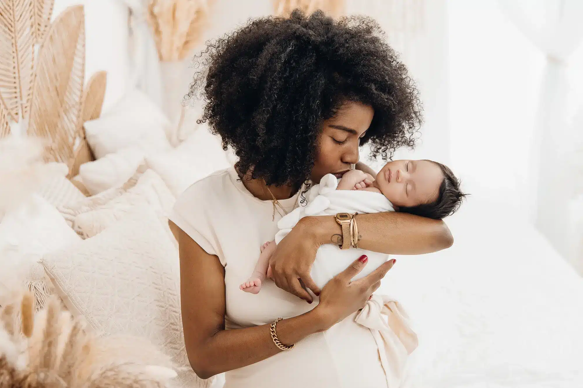 Jeune mère noire tenant son nouveau-né enveloppé dans une couverture blanche, dans un décor doux et lumineux, ambiance cocooning.