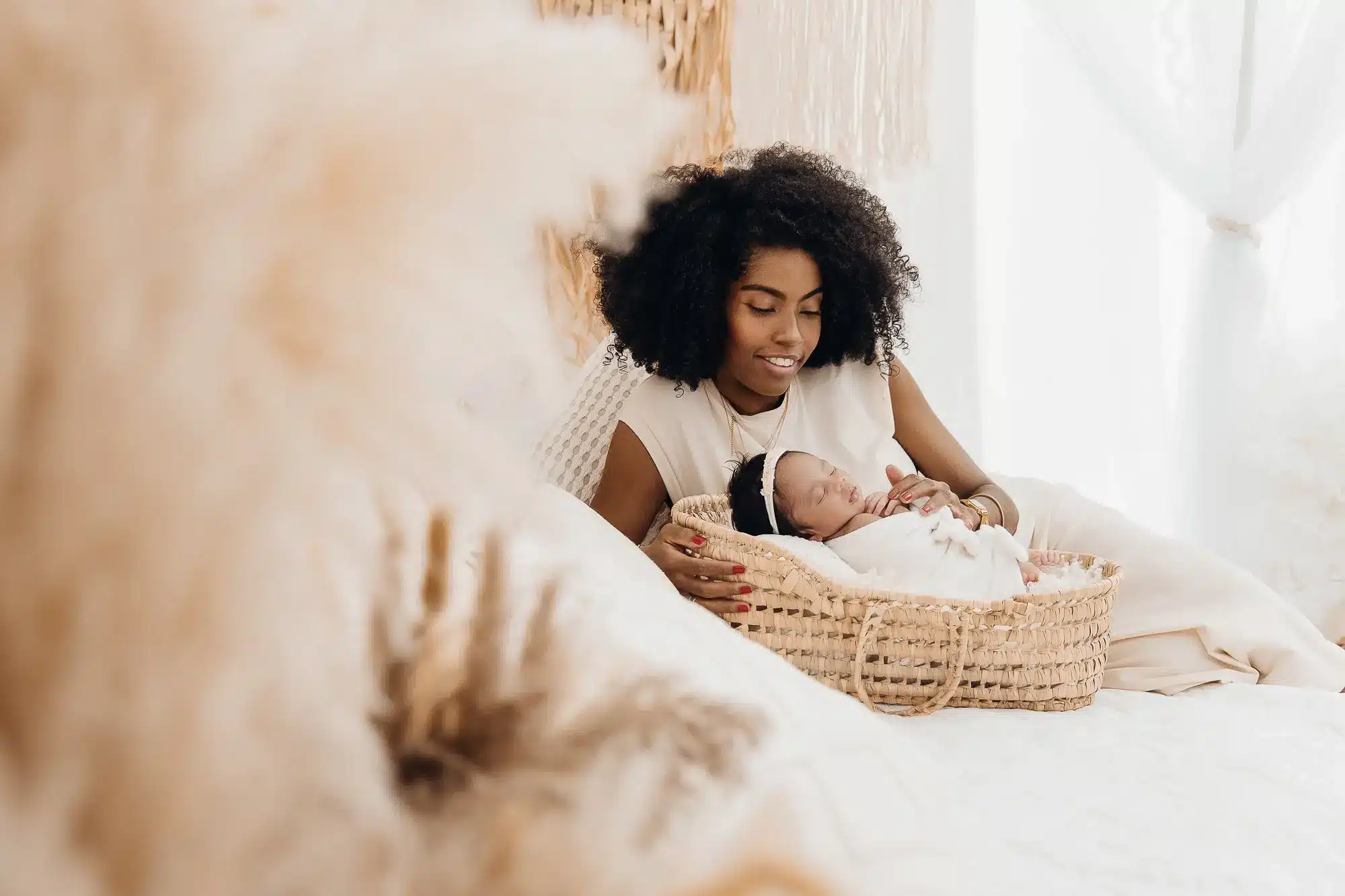 Mère souriante près d’un bébé endormi dans un couffin en osier, ambiance lumineuse et douce, intérieur cosy et naturel.