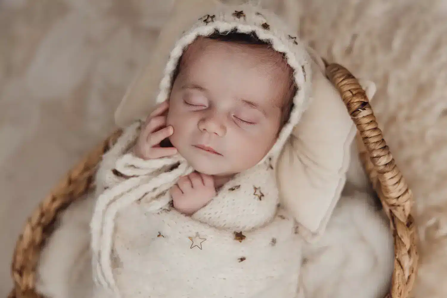 Nouveau-né endormi dans un panier tressé, bonnet et couverture doux étoiles, gestes délicats et ambiance chaleureuse. La sécurité en séance photo nouveau-né.