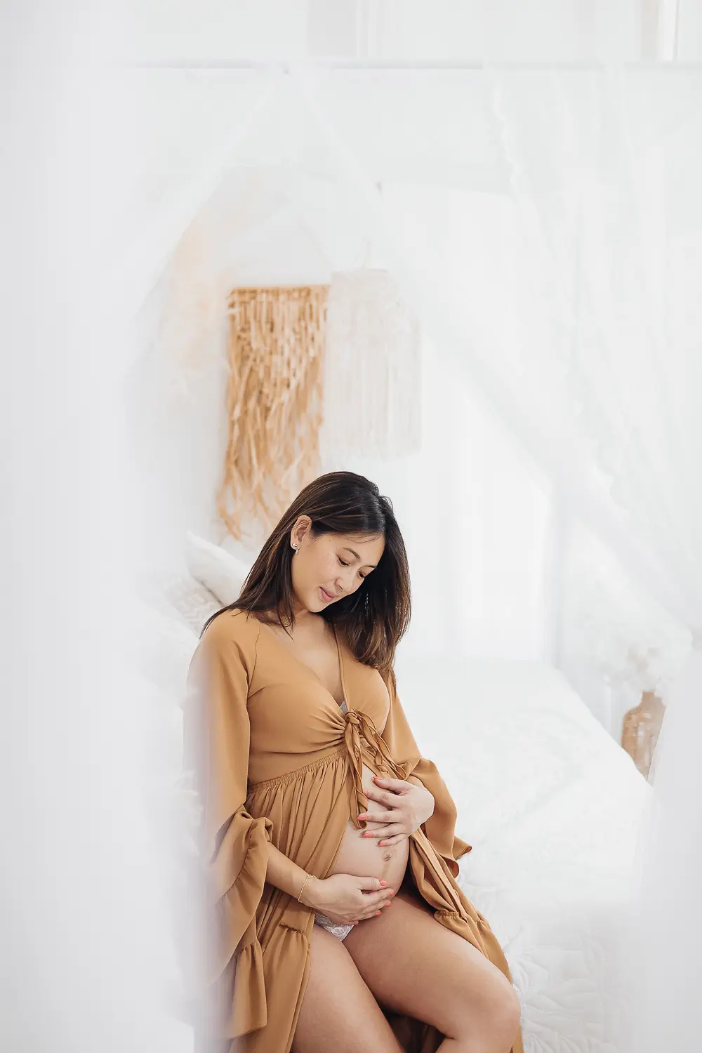 Allaitement et grossesse: femme enceinte dans un studio blanc, vêtement ample beige, main sur ventre.