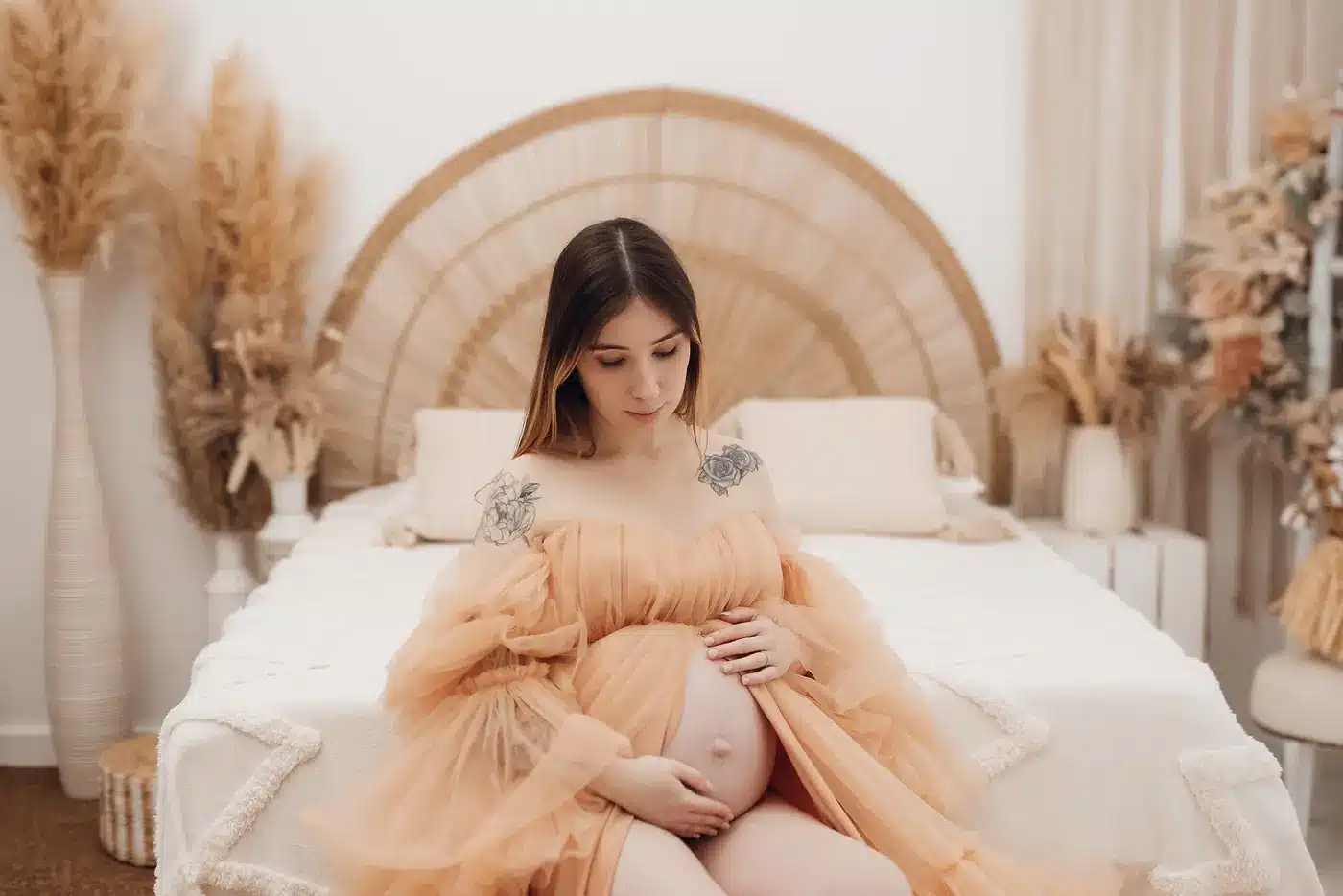 Future maman assise sur un lit bohème au studio, séance grossesse dans un décor clair